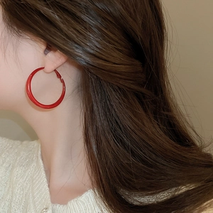 Detailed view of large retro red glossy hoop earrings worn by a model in warm light