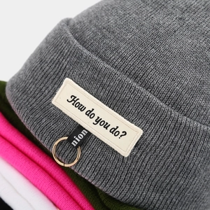 Bonnet en maille gris avec anneau métallique et écusson de lettres pour un style urbain