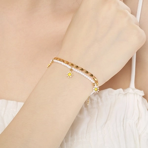 Detail of double-layer bracelet with gold chain, white beads and daisy charms on wrist
