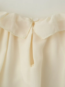 Dettaglio camicetta in chiffon crema con colletto a balze e chiusura con bottone posteriore