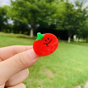 Close-up of a cute red tomato hair clip with a smile face and green leaf detail
