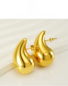 Macro detail of high-polish gold hollow teardrop earrings on a textured white surface