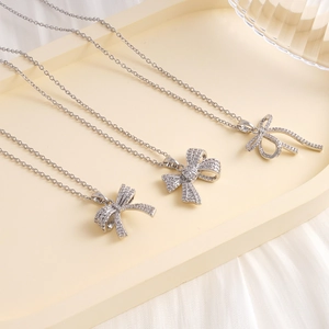 Elegant silver bow necklaces with sparkling zircons on a soft beige display tray