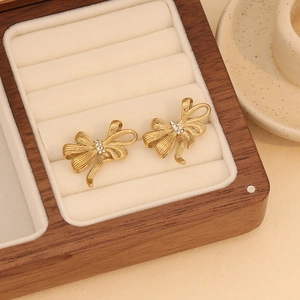 Detail of golden bow earrings with textured finish and small crystals on beige velvet
