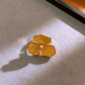 Detailed close-up of golden flower ring with textured petals and clear gemstone