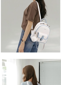 Detail view of white and blue mini backpack with plush ball charm and metal buckle on model
