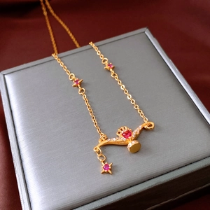Close-up of a 24K gold-plated necklace featuring a starburst and red heart crown pendant