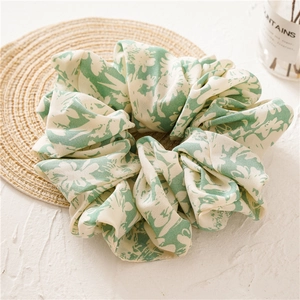 Detail view of large green floral fabric scrunchie on a woven coaster with soft lighting