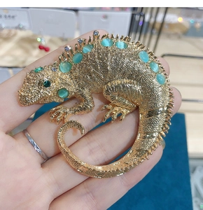Detailed view of chameleon brooch with green cat-eye stones and crystal accents on gold alloy