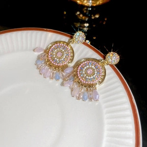 Macro detail of golden dreamcatcher earrings with pink gems and beaded tassels on a plate