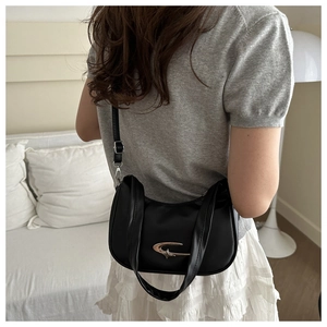 Close-up of black leather underarm bag featuring a silver crescent metal buckle on a model