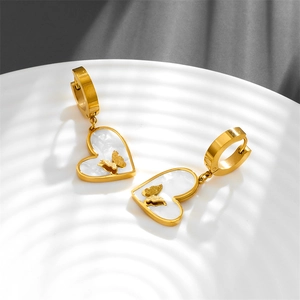 Golden heart-shaped shell earrings with butterfly relief on white textured background
