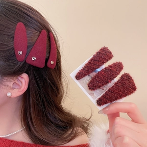 Detail of plush burgundy triangular hair clips with metallic B buckle on tweed fabric