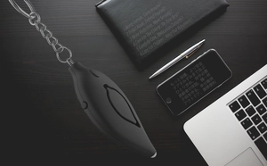 Detail of leaf-shaped personal alarm with metal keychain on a dark wooden desk