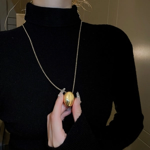 Elegant gold geometric oval pendant necklace on black sweater for modern women