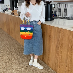Detail of handmade rainbow knit bag featuring white cloud accents and colorful pom-poms