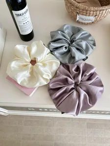 Detailed view of three oversized silk satin scrunchies in white, grey, and purple