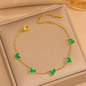 Detail of 18K gold bracelet with five green heart charms on jewelry box