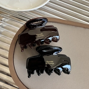 Close-up of gloss shark hair clips in coffee and black with gold lettering detail