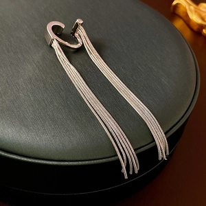 Detail showing elegant silver metal tassel ear cuff with long chains on a black display stand