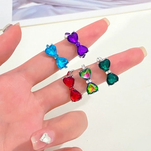 Close-up of heart-shaped crystal butterfly rings in five vibrant colors on hand