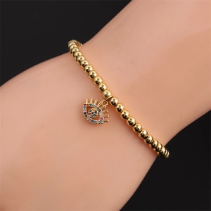 Detail of gold beaded bracelet with colorful zircon evil eye charm worn on wrist