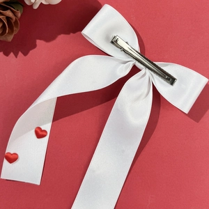 Elegant white satin bow hair clip with red hearts on a vibrant red background