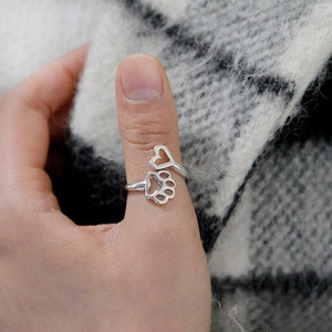Close-up of adjustable silver ring with hollow dog paw and heart design on model thumb