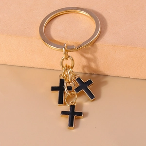 Detail of gold keychain with three black enamel cross pendants on geometric background