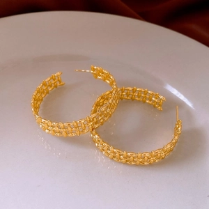 Detailed view of gold plated C-shaped hoop earrings with woven chain texture on white plate