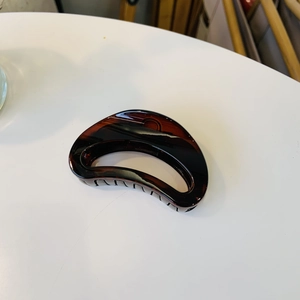 Close-up of a semi-circular amber tortoiseshell hair claw clip with a glossy resin finish