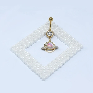 Dettaglio del piercing all'ombelico dorato con ciondolo a pianeta rosa e pietre di zircone