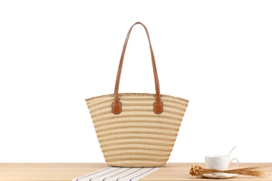 Detail of striped woven beach tote featuring beige straw texture and brown leather straps