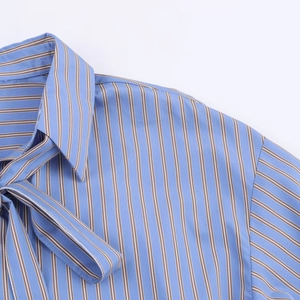 Detalle de camisa de rayas azules y marrones con lazo en el cuello y textura tejida