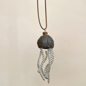 Macro detail of jellyfish-shaped pendant necklace with pearl tassels and rustic texture
