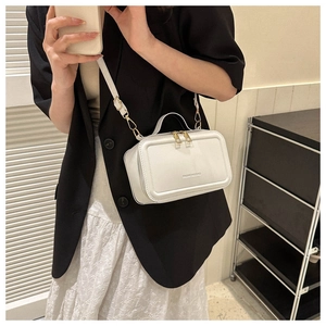 White mini suitcase-style crossbody bag with gold chain and top handle shown on model