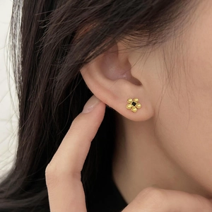 Elegant gold flower stud earrings with black gemstone center on a female model