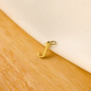 Detailed view of a gold letter J pendant on light wood and white textile background