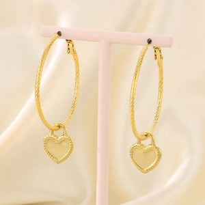 Detail of gold heart lock pendant on twisted rope earrings on a pink jewelry stand