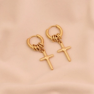 Detail of gold cross hoop earrings on elegant pink fabric with polished metal finish