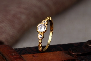 Macro detail of a gold lace ring with three clear zircons on a vintage wooden box