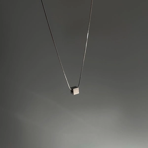 Macro shot of silver cube pendant on a sleek snake chain necklace with metallic finish