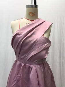 Detailed close-up of pink satin one-shoulder evening gown with waist embroidery and pleats