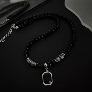 Dettaglio della collana di perle nere con pendente nero quadrato e accenti in metallo
