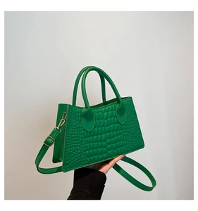 Detail of green crocodile pattern handbag with dual handles and adjustable strap