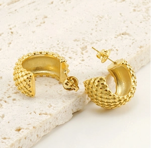 Detailed close-up of golden C-shaped earrings with vintage dotted texture on stone base