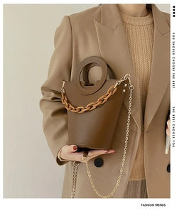 Detail of brown bucket bag with amber resin chain and metallic strap on model