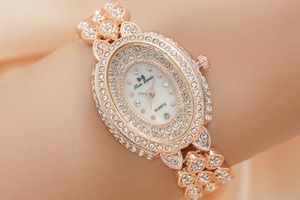 Close-up of rose gold women's watch with shimmering crystals and oval dial on wrist