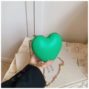 Detail of green heart-shaped mini bag with golden metal chain strap and matte texture