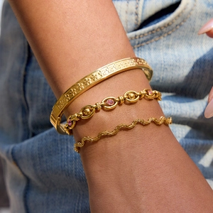 Gros plan de bracelets dorés superposés avec texture florale mate et pierres roses